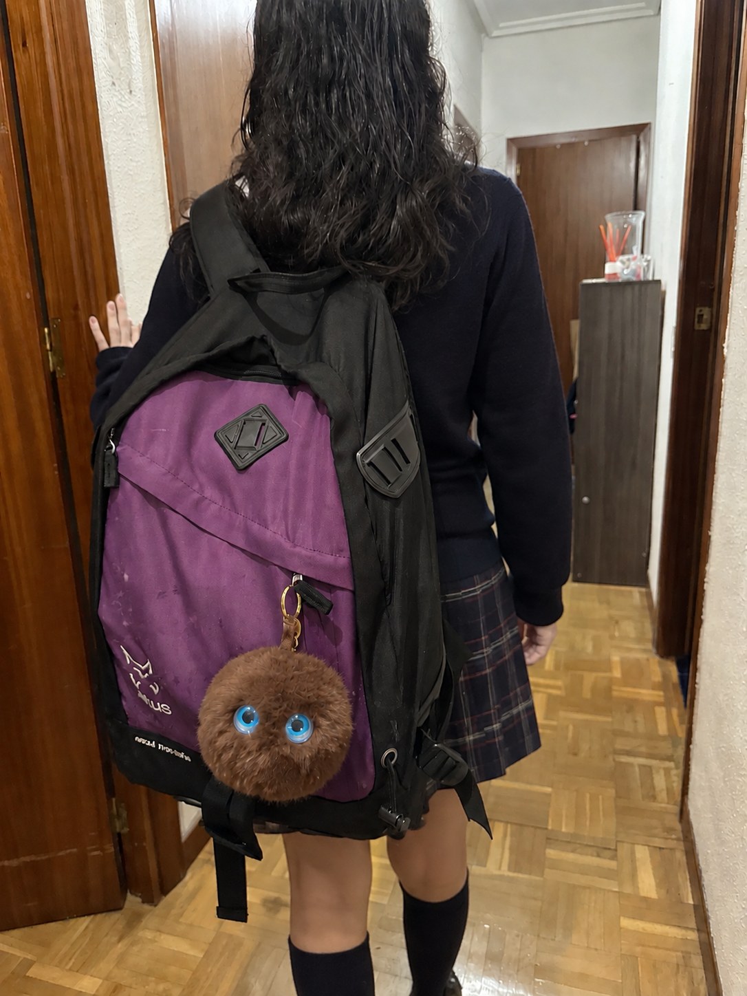 niña con uniforme saliendo hacia el cole con un mimu marrón colgado de la mochila